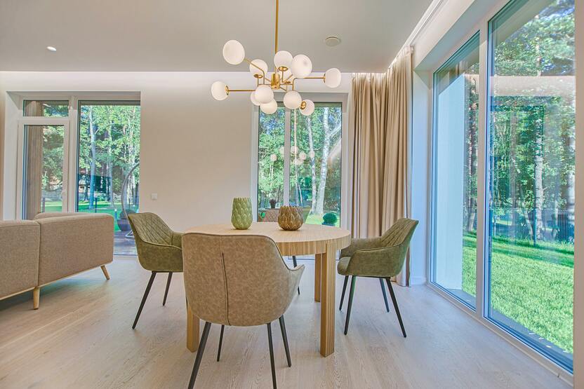 Sitzbereich Wohnzimmer Runder Holztisch mit grünen und beigen Stühlen auf hellem Holzboden vor Fensterfront